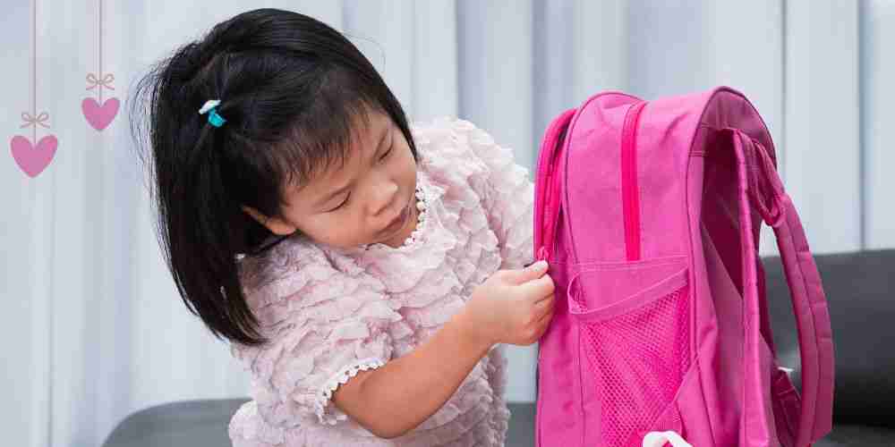 a preschool aged child zipping up her pink backpack