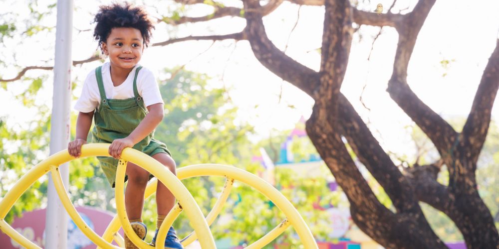 child playing outdoors on a yellow structure with a tree in the background