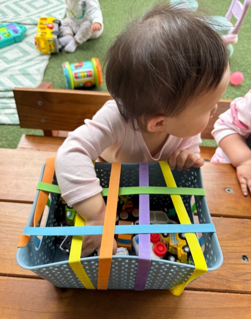infant reaching into a treasure basket with soft elastic straps and toys inside